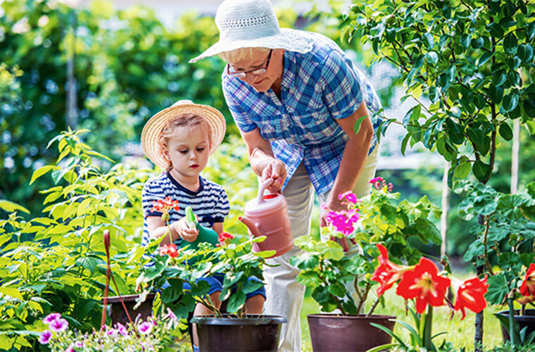 grandmother watering flowers in garden with grandchild
