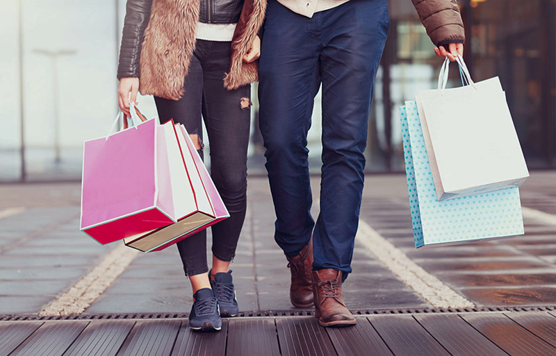 two people walking down sidewalk with shopping bags in arms
